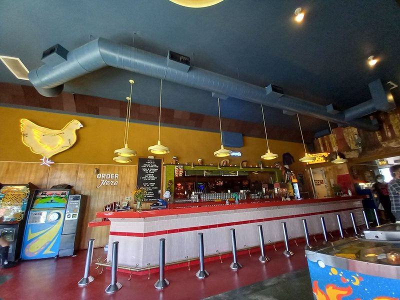 Inside: the neon chicken over the bar, the Order Here sign, the taps, and pinball machines along the wall