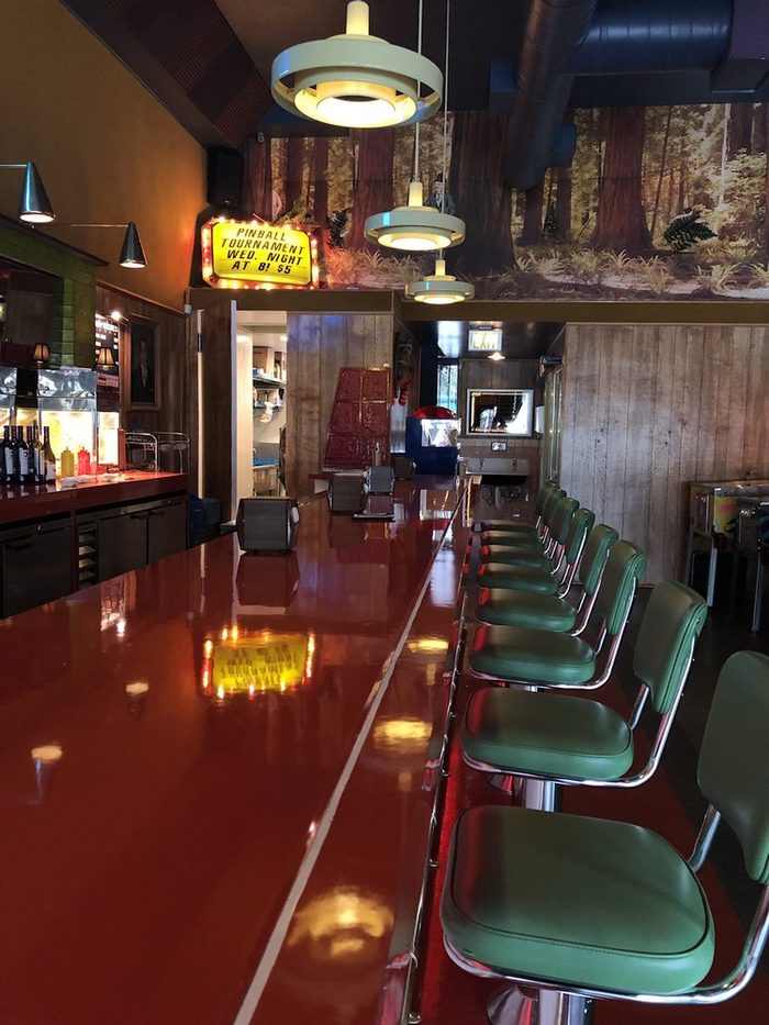 The red bar counter and green stools, with our lit pinball tournament sign above the doorway