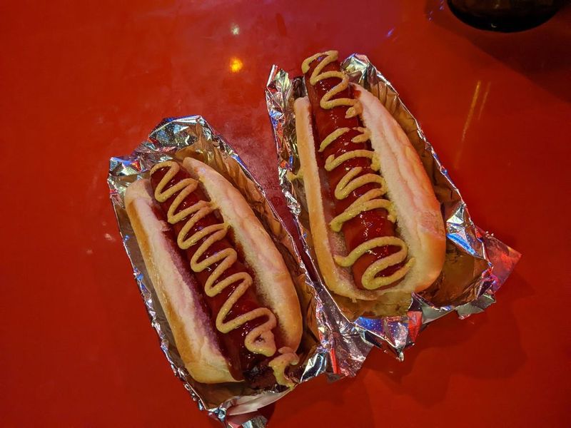 Two hot dogs in foil with mustard zigzags on a red checkered tray