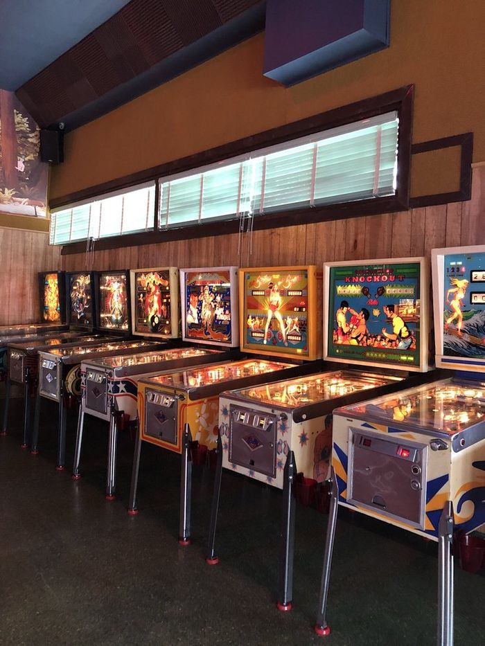 A row of lit vintage pinball machines along the wall