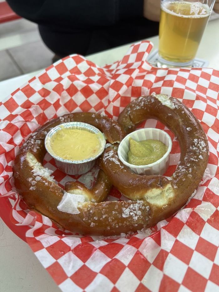 A hot pretzel on checkered paper with cups of nacho cheese and mustard